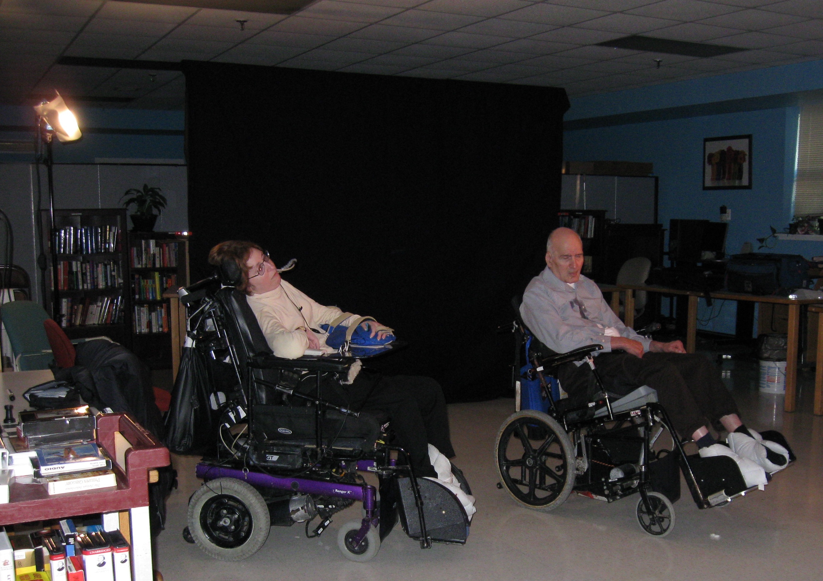 Ilene Myers and Robinson Fredenthal sit in wheelchairs before a black backdrop.