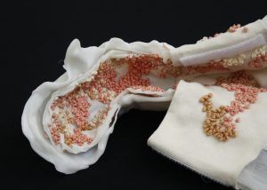A close shot of a L-shaped wrist braces with curvy plastic wedges. The braces’ interior is lined with a soft and creamy fabric embroidered with clusters of white and pinkish French knots (tiny ball shaped stitches).