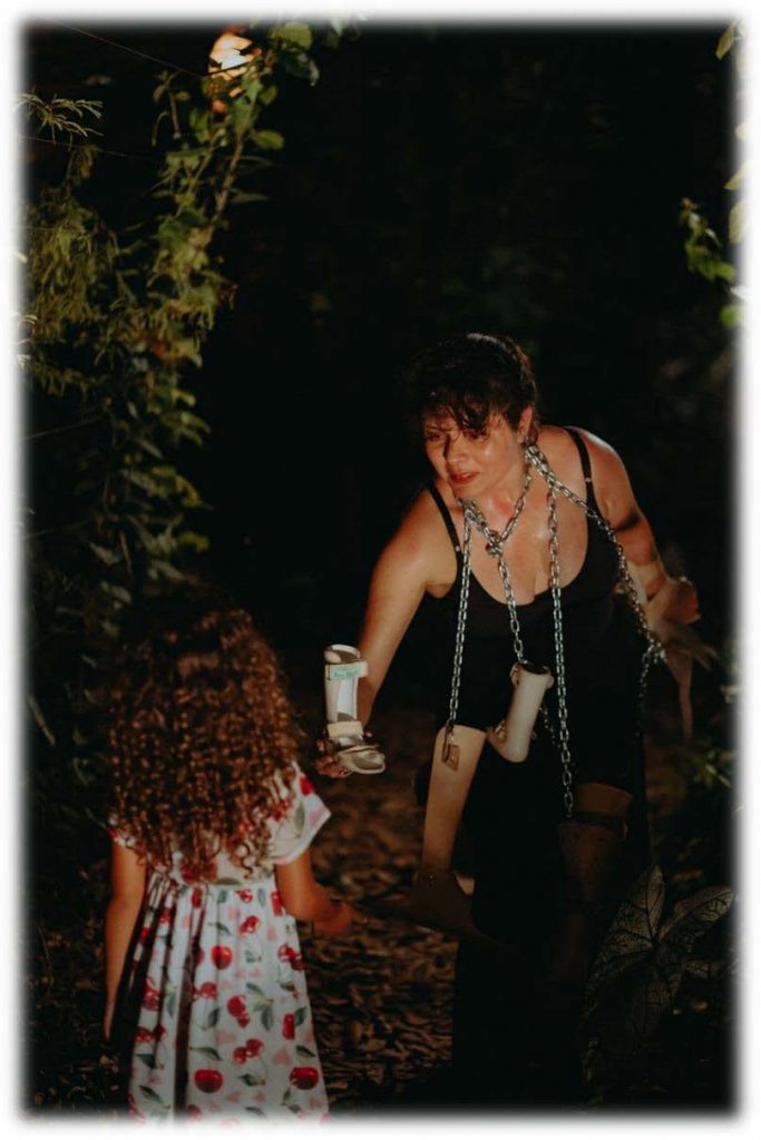 I'm in a garden, at night… I am standing in performance and wearing several orthosis hangings by chains tied around my neck. I offer a kind of child orthosis to a little girl who approaches me with big curly hair and a floral dress. In the background several plants of different sizes compose the scenery of this improvised scene during a Brazilian artists’ event.