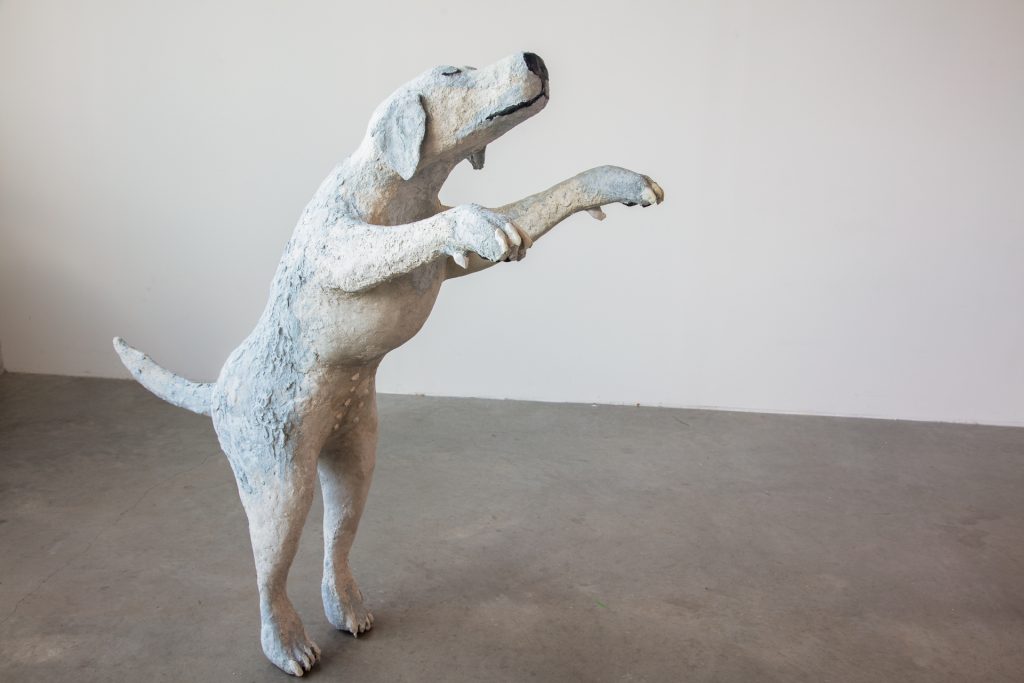“Dancing with London I.” A frontal view of one of the sculptures of the dogs. You can see that the dog’s belly has nipples, and the nails of her claws are shiny and white. The expression on the dog’s face is serene, her eyes are closed and she has a hint of a smile.