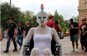 In this series, I documented inaccessible parts of my college campus while dressed as our mascot. The first photo in the series is in color. It shows myself using my wheelchair in a busy crowd of USC fans before a football game. I painted myself white to highlight how the Tommy Trojan mascot is rooted in values of ableism and white supremacy, so my white body stands out against the blacks, reds, and golds of the sports fans’ attire.