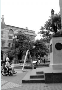 In this series, I documented inaccessible parts of my college campus while dressed as our mascot. I am in my wheelchair sitting across from the famous statue of Tommy Trojan. The statue is elevated on a very tall pedestal, forcing me to look up at it. There are also stairs in front of the pedestal, which would prevent me from being able to approach it closely. The lack of color in the photo highlights the timeless idea of able bodies being elevated above disabled bodies.