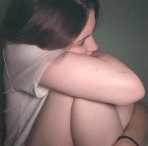 In this photo, I wanted to express parts of my experience as an autistic person. I am sat in front of my green bedroom wall in dim lighting. I am showing a side view of my white t-shirt, reddish-brown hair, white face, arms and legs. I seek comfort by holding my arms around my body. I have twisted and pressed my limbs close to my body to represent societal pressures and judgment. My brown eyes are looking directly ahead as I avoid eye contact with the viewer. In this moment, I think on the unwritten rules I’m supposed to decipher and my fear of misunderstandings. 