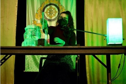 the image is tinted by vibrant green light. lauren sitting and holding a copy of her book, like a dog. they are slowing lowering the book into the vase that is filled with dirt.